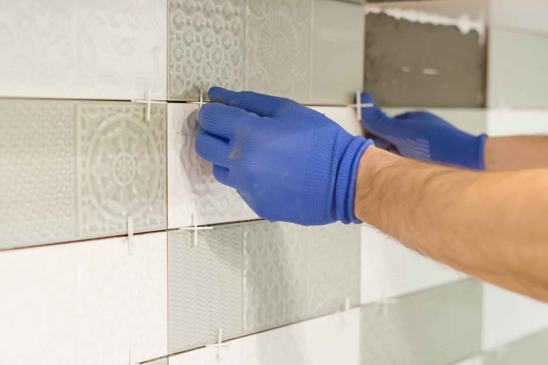 Installer in gloves setting white wall tile